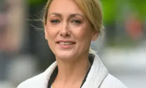 Portret uśmiechniętej blondynki w jasnym płaszczu.
