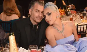Lady Gaga i Christian Carino blisko siebie przy stole, ona w błękitnej sukni i biżuterii, on w czarnym garniturze.