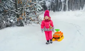 Mała influencerka w zimowym lesie ciągnie zabawkę. Zastanawiasz się, ile zarabiają dzieci influencerów za udział w kampaniach reklamowych?