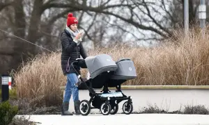 Kobieta w czerwonej czapce prowadzi podwójny wózek, który mógłby znaleźć się w rankingu najdroższych wózków dziecięcych używanych przez polskie gwiazdy.