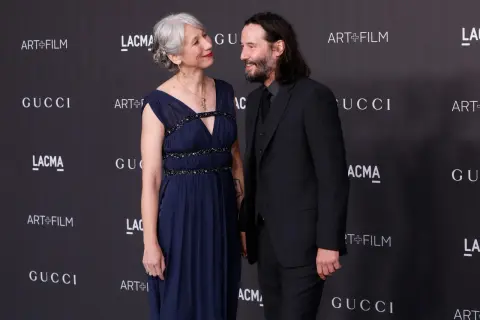 Keanu Reeves i jego żona Alexandra Grant patrzą na siebie z uśmiechem na tle logo Gucci i Art+Film.