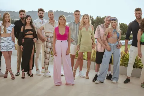 Grupa młodych ludzi pozuje do zdjęcia. Widać ich stroje, uśmiechy, ale czego nie widać w kamerach podczas nagrań reality show?
