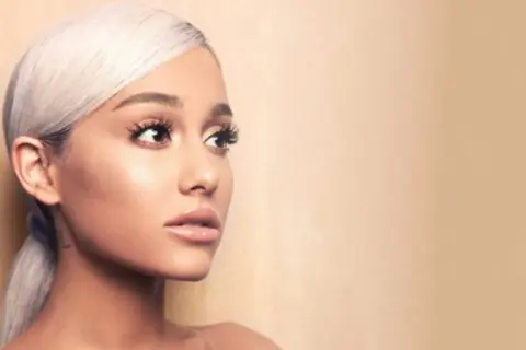 Portret Ariany Grande z blond włosami spiętymi w kucyk, patrzącej w bok.