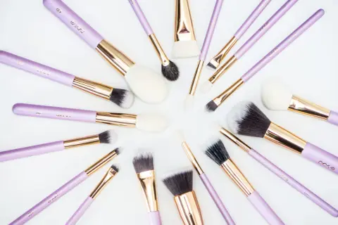 Recenzja pędzli do makijażu które poleca każda polska beauty-influencerka. Fioletowe pędzle z złotymi okuciami ułożone na białym tle.