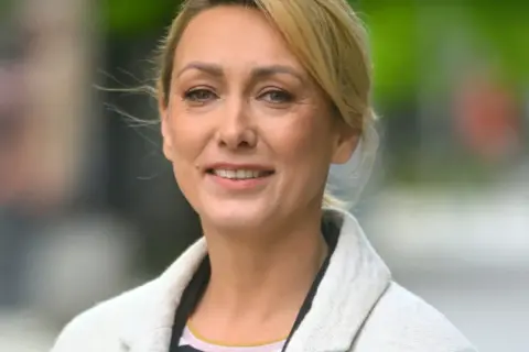 Portret uśmiechniętej blondynki w jasnym płaszczu.