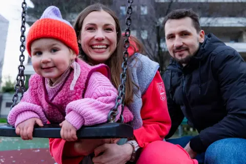 Rodzina na placu zabaw. Dziecko w różowym sweterku i czapce, obok uśmiechnięta mama i tata. To przykład listy dzieci gwiazd, które pracują w zwykłych zawodach poza branżą.