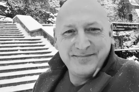 Jacek Wójcik, w zimowej scenerii, na tle zaśnieżonych schodów. Wiek nie jest widoczny, ale uśmiech sugeruje radość.
