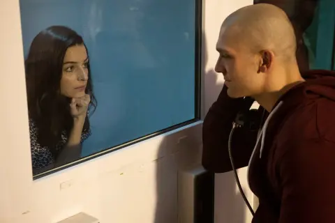 Tomasz Chada rozmawia przez telefon z żoną, która patrzy na niego przez szybę.