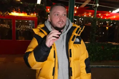 Książulo w żółtej kurtce przed restauracją Carmines, gdzie jego recenzja obiadu była negatywna.