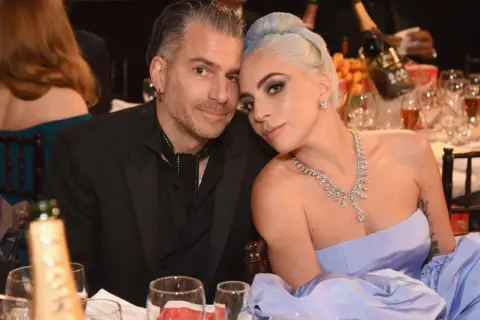 Lady Gaga i Christian Carino blisko siebie przy stole, ona w błękitnej sukni i biżuterii, on w czarnym garniturze.