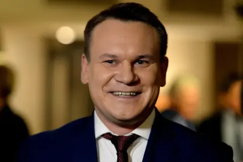 Uśmiechnięty mężczyzna w garniturze, z krawatem. Czy Tarczyński jest żonaty? To pytanie, na które odpowiedź może być ukryta w jego spojrzeniu.