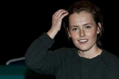 Olga Frycz, młoda kobieta z piegami, uśmiecha się, poprawiając włosy. Na jej dłoni plaster.