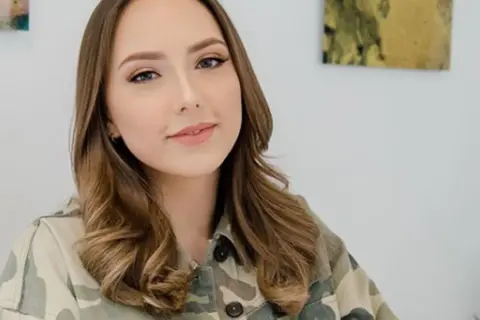 Uśmiechnięta Hailie Jade Scott Mathers w kurtce moro, z lekko pofalowanymi brązowymi włosami.