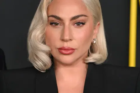 Lady Gaga, z blond włosami i makijażem, w czarnej marynarce. Czy Lady Gaga ma dziecko? To pytanie nurtuje fanów.