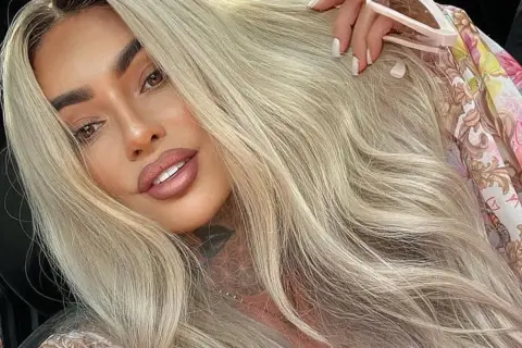 Ania Królowe Życia z blond włosami i tatuażem na szyi, w kwiecistej bluzce.