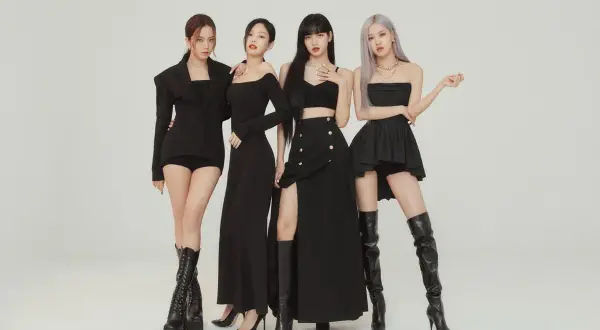 Cztery członkowie BLACKPINK w czarnych, stylowych strojach pozują do zdjęcia.