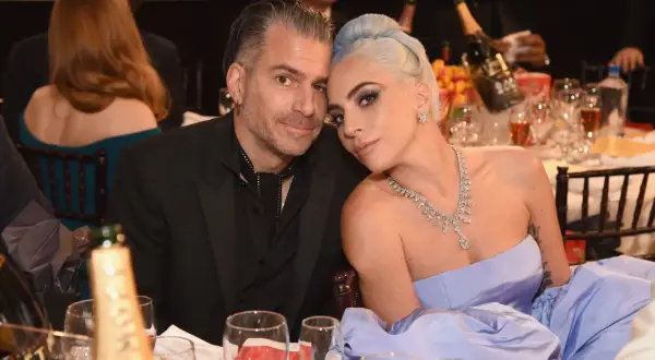 Lady Gaga i Christian Carino blisko siebie przy stole, ona w błękitnej sukni i biżuterii, on w czarnym garniturze.