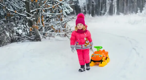 Mała influencerka w zimowym lesie ciągnie zabawkę. Zastanawiasz się, ile zarabiają dzieci influencerów za udział w kampaniach reklamowych?