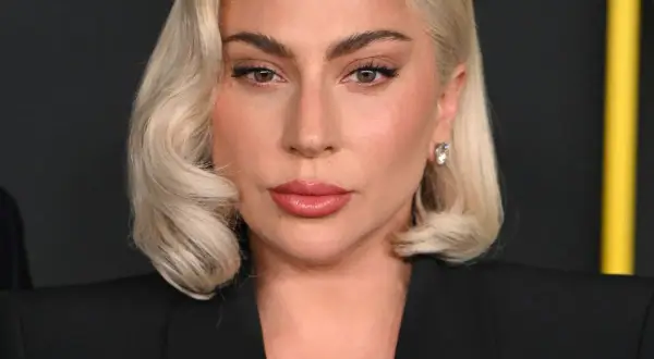 Lady Gaga, z blond włosami i makijażem, w czarnej marynarce. Czy Lady Gaga ma dziecko? To pytanie nurtuje fanów.