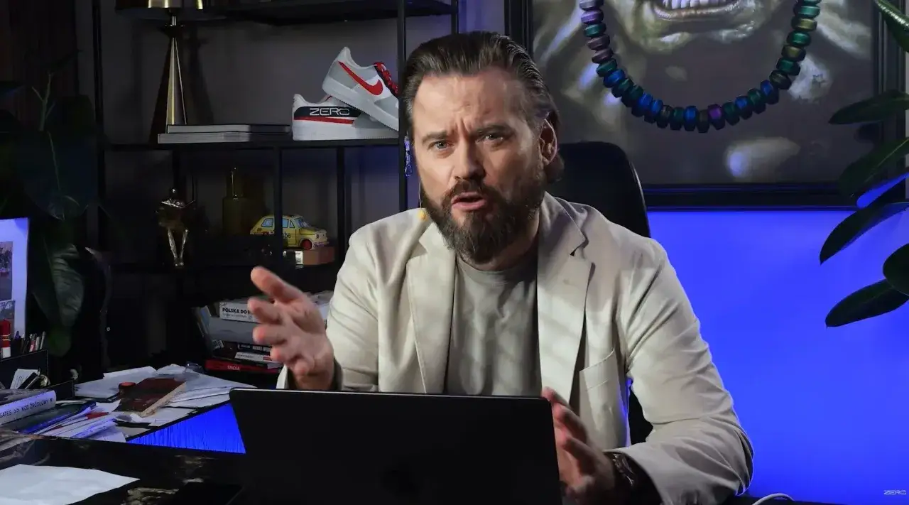 Mężczyzna w beżowej marynarce, z brodą, opowiada o tym, kto stoi za nowym tajemniczym projektem największych gwiazd polskiego yt.