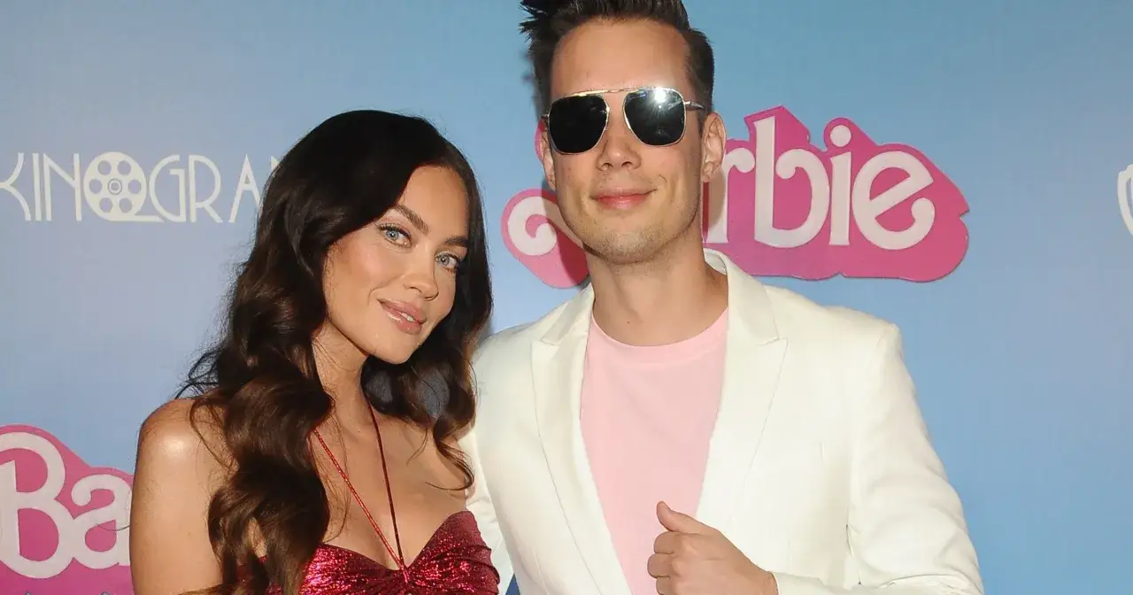 Edyta Zając z partnerem na ściance Barbie. Ona w błyszczącej sukience, on w białej marynarce i różowej koszulce.