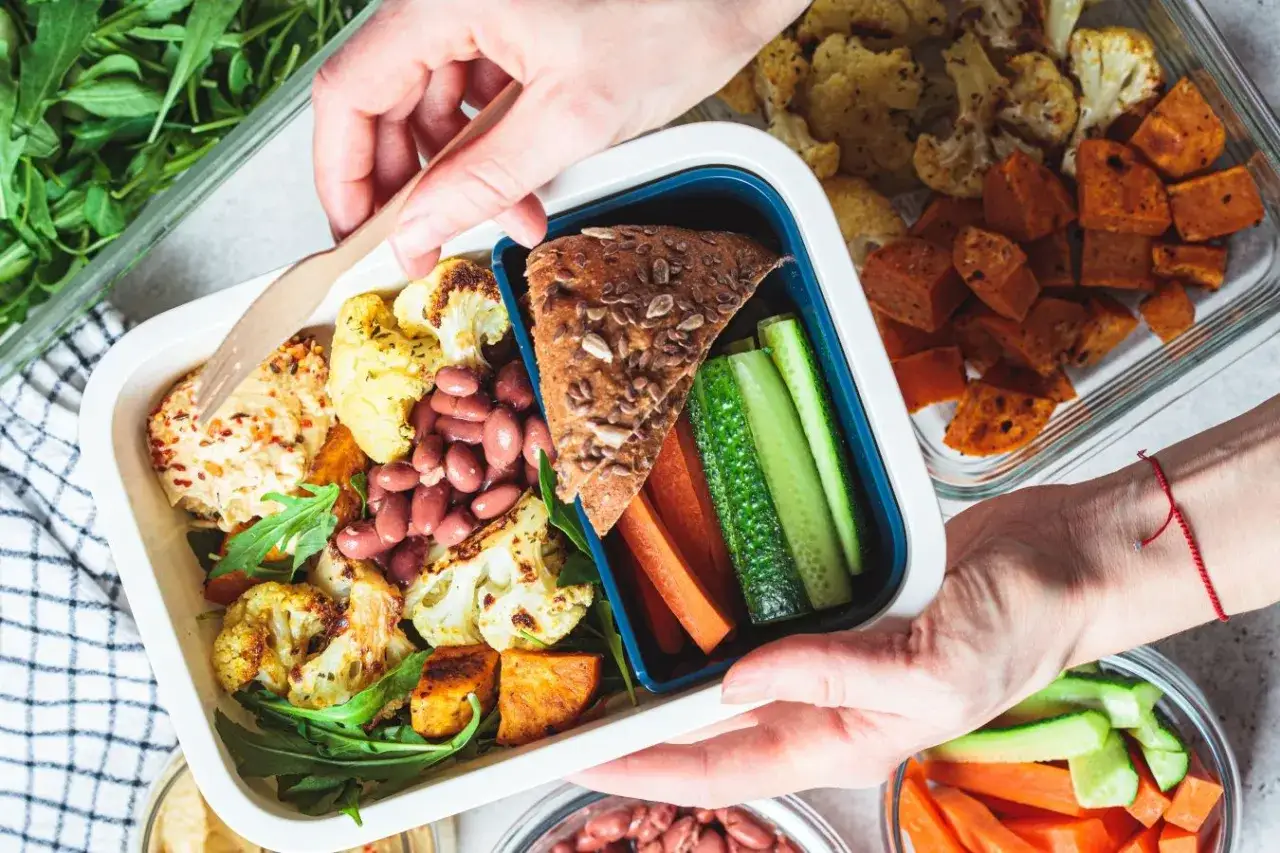 Czy warto kupić catering dietetyczny od najpopularniejszej trenerki fitness? Pudełko z kolorowym, zdrowym jedzeniem: pieczony kalafior, fasola, warzywa, chleb.