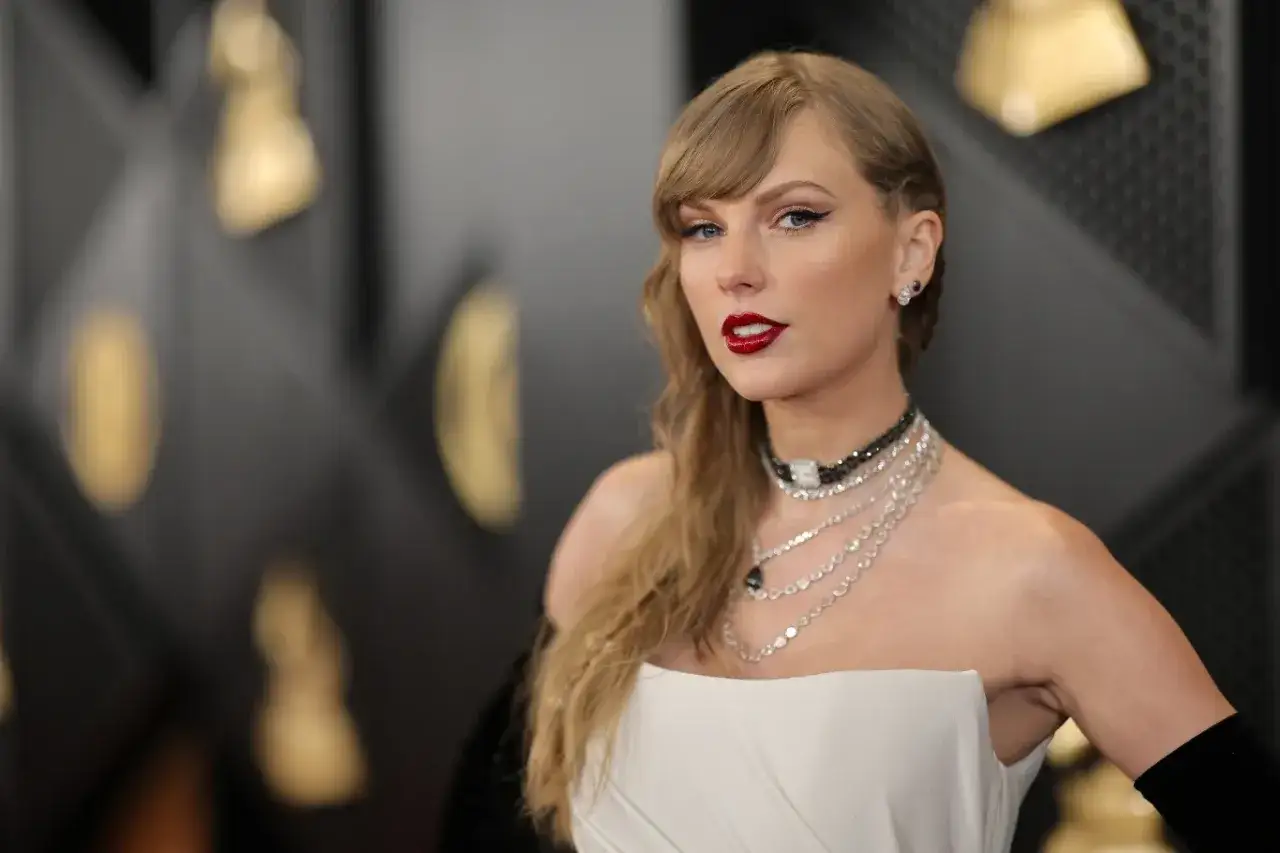 Taylor Swift w białej sukni i biżuterii, z mocnym makijażem. W tle złote elementy, przypominające nagrody. Może to symbolizować jej walkę o prawa do utworów po sporze z byłym menedżerem.