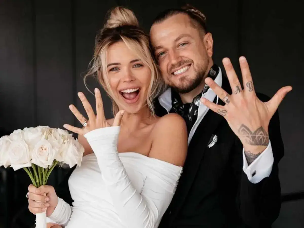 Sandra Kubicka i Baron świętują, pokazując obrączki. Uśmiechnięci, w białej sukni i czarnym garniturze, z bukietem róż.
