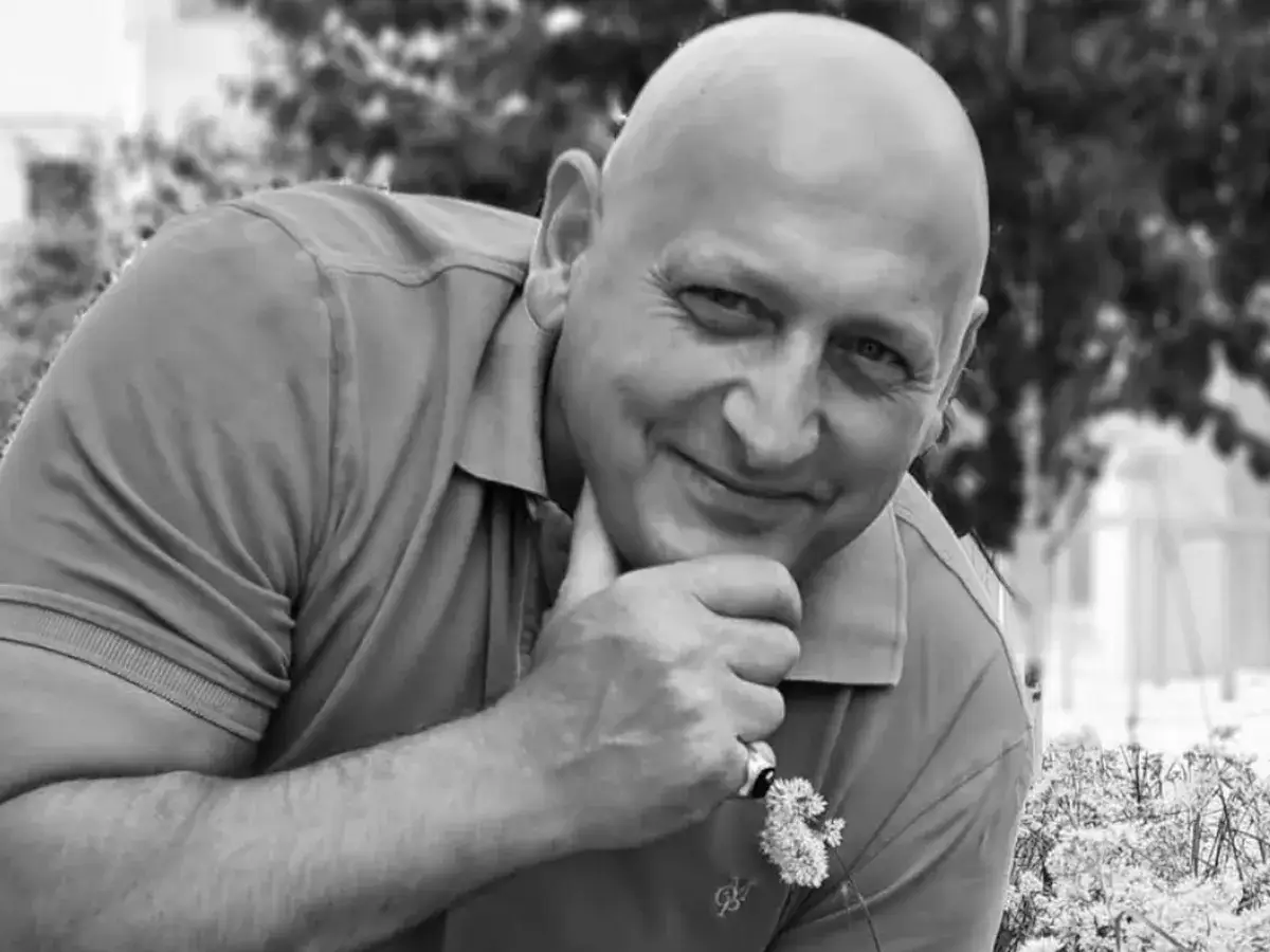 Uśmiechnięty Jacek Wójcik, jego wiek zdradza doświadczenie. Dłoń podtrzymuje podbródek, na palcu pierścionek z kwiatkiem.