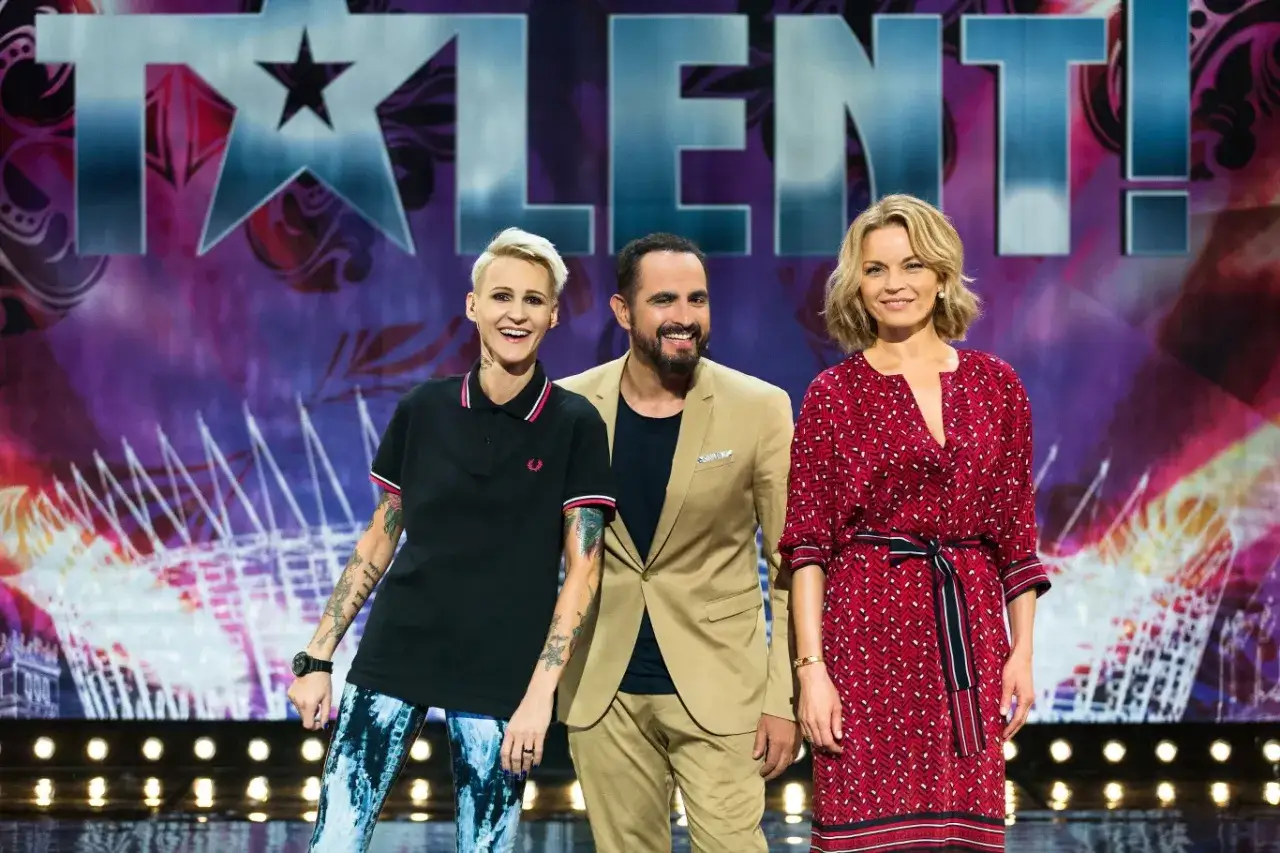 Trzech jurorów talent show, uśmiechniętych na tle logo programu. Czy to tylko pozory, dlaczego jurorzy programów talent show nie lubią się prywatnie?