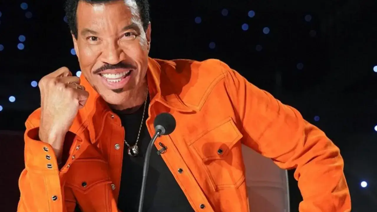 Lionel Richie w pomarańczowej kurtce, uśmiechnięty, zaciśnięta pięść. Czy to jego sposób na pokazanie, dlaczego jurorzy programów talent show nie lubią się prywatnie?