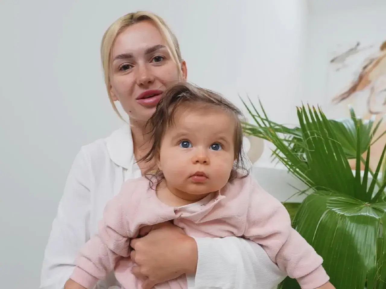 Uśmiechnięta blondynka trzyma dziecko. Czy to które dzieci gwiazd zadebiutowały w reklamach jeszcze jako noworodki?