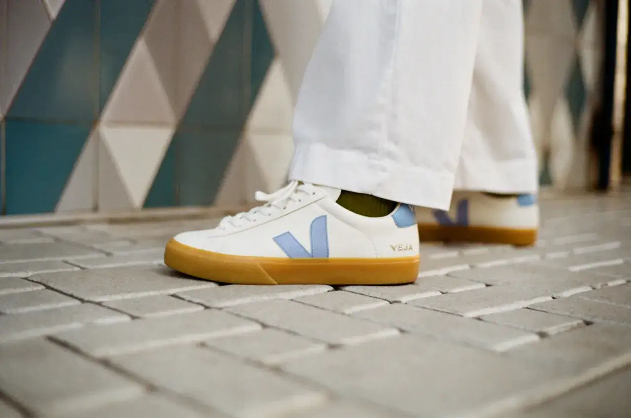 Szczera opinia o butach VEJA, które promuje najpopularniejsza polska szafiarka. Białe sneakersy z błękitnym logo i gumową podeszwą na tle geometrycznych płytek.