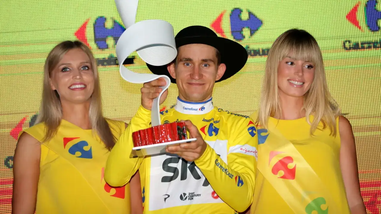 Michał Kwiatkowski, piosenkarz, w żółtej koszulce z pucharem i kobietami w żółtych sukienkach.