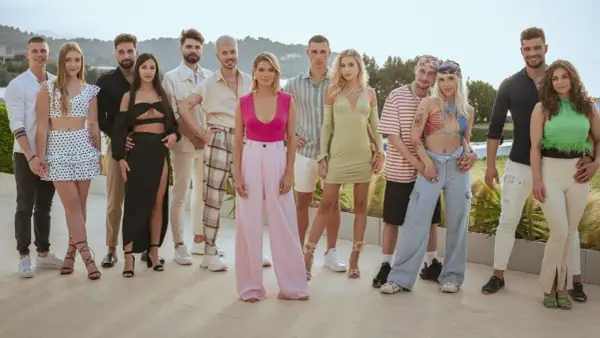 Grupa młodych ludzi pozuje do zdjęcia. Widać ich stroje, uśmiechy, ale czego nie widać w kamerach podczas nagrań reality show?