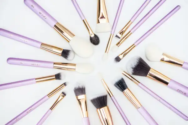 Recenzja pędzli do makijażu które poleca każda polska beauty-influencerka. Fioletowe pędzle z złotymi okuciami ułożone na białym tle.