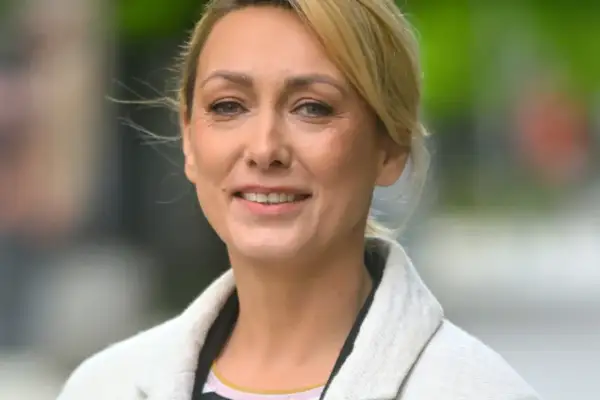 Portret uśmiechniętej blondynki w jasnym płaszczu.