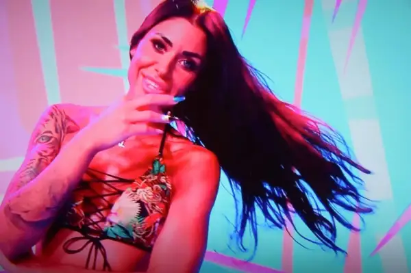Stella z Love Island w kolorowym bikini, z tatuażem tygrysa na ramieniu, uśmiecha się do kamery.
