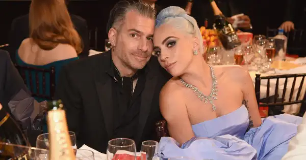 Lady Gaga i Christian Carino blisko siebie przy stole, ona w błękitnej sukni i biżuterii, on w czarnym garniturze.