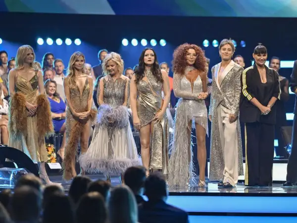 Uśmiechnięci tancerze z programu "Taniec z Gwiazdami" w błyszczących kreacjach pozują na scenie.